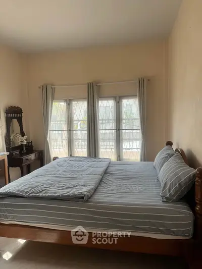 Cozy bedroom with large windows and elegant wooden furniture, perfect for relaxation.