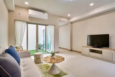 Modern living room with stylish furniture and large TV, featuring a garden view through sliding glass doors.