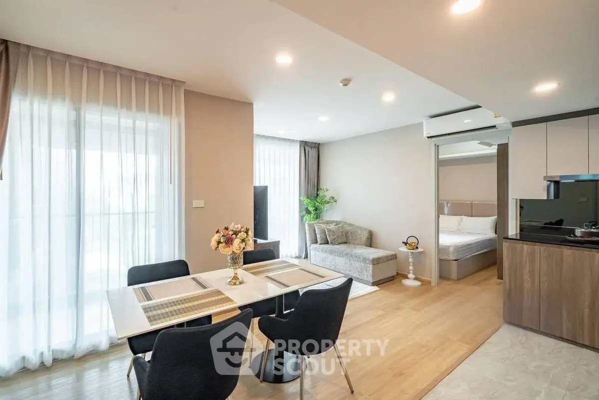Modern open-plan living room with dining area and bedroom, featuring elegant decor and natural light.
