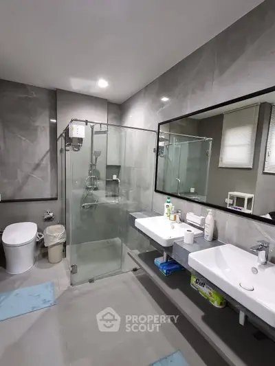 Modern bathroom with glass shower, dual sinks, and sleek gray tiles.