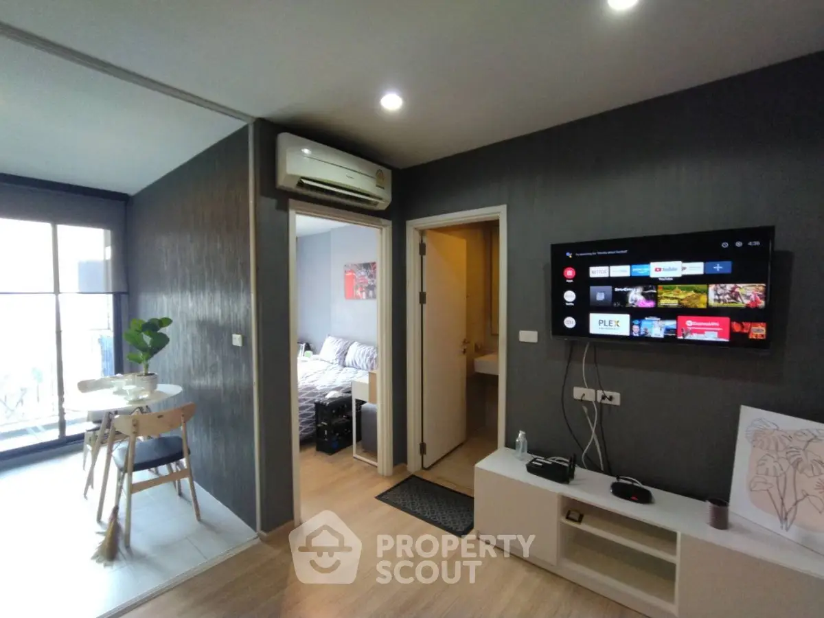 Modern apartment interior with open living area and wall-mounted TV, featuring a cozy dining space and bedroom access.