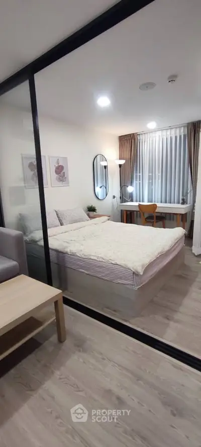 Modern bedroom with glass partition, cozy decor, and natural light.