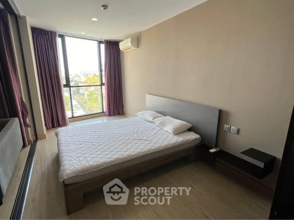 Spacious bedroom with large window and modern furnishings in a stylish apartment.