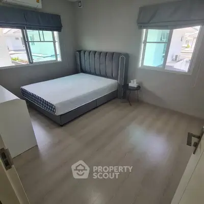 Spacious bedroom with modern decor and ample natural light from two windows.