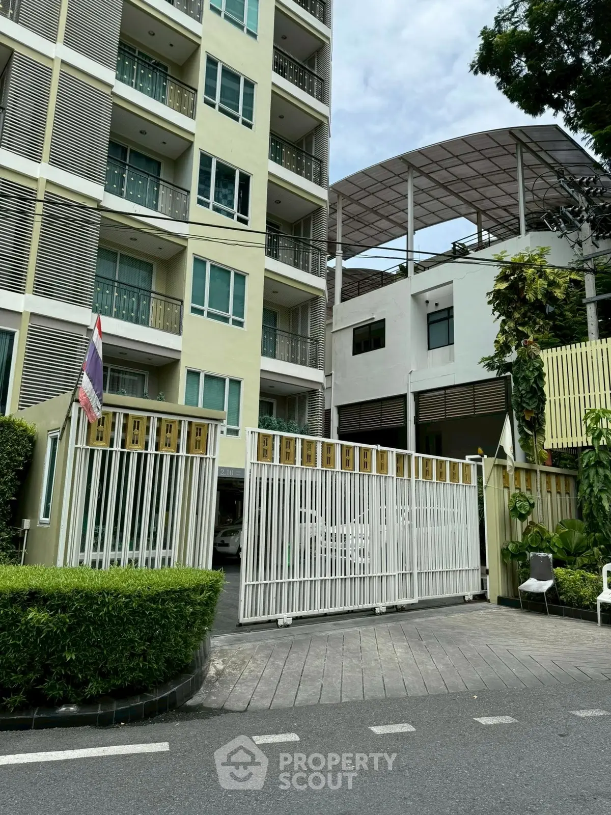 Modern apartment building exterior with gated entrance and lush greenery.