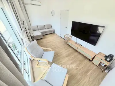 Modern living room with large TV, stylish furniture, and natural light from big windows.