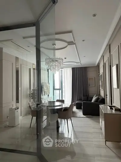 Luxurious modern living room with elegant chandelier and glass partition, featuring stylish furniture and natural light.