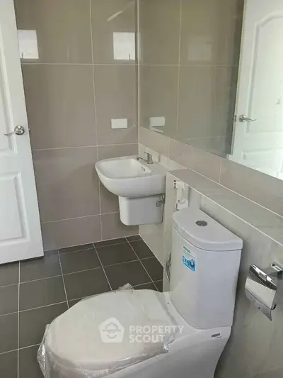 Modern bathroom with sleek fixtures and neutral tiles, featuring a compact sink and toilet.