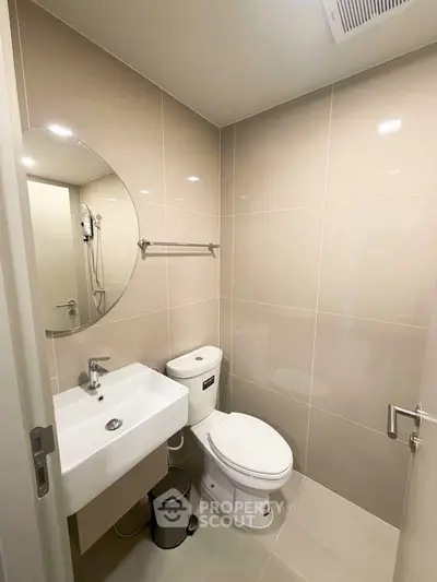 Modern bathroom with sleek fixtures and neutral tiles, featuring a round mirror and compact design.