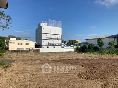 Vacant land with a modern white building in a suburban area under a clear blue sky.