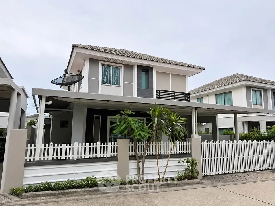 Modern two-story house with white picket fence and spacious driveway in suburban neighborhood.