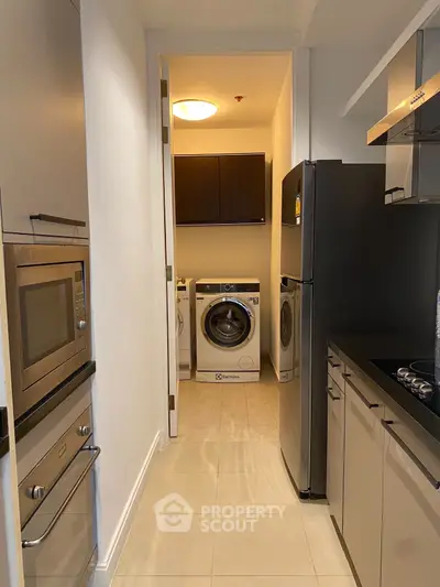 Modern kitchen with sleek appliances and laundry area, featuring a washing machine and microwave.