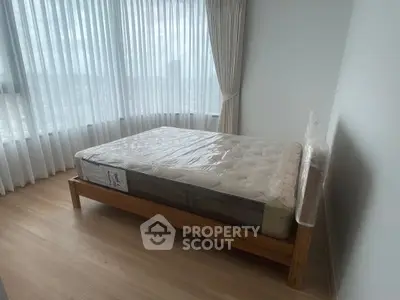 Spacious bedroom with large windows and natural light, featuring a new mattress on a wooden bed frame.