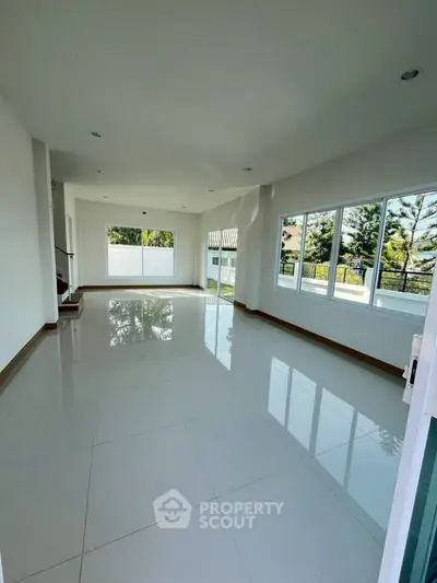 Spacious sunlit living room with large windows and glossy white tiles