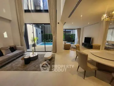 Luxurious open-plan living room with pool view, elegant furniture, and high ceilings.