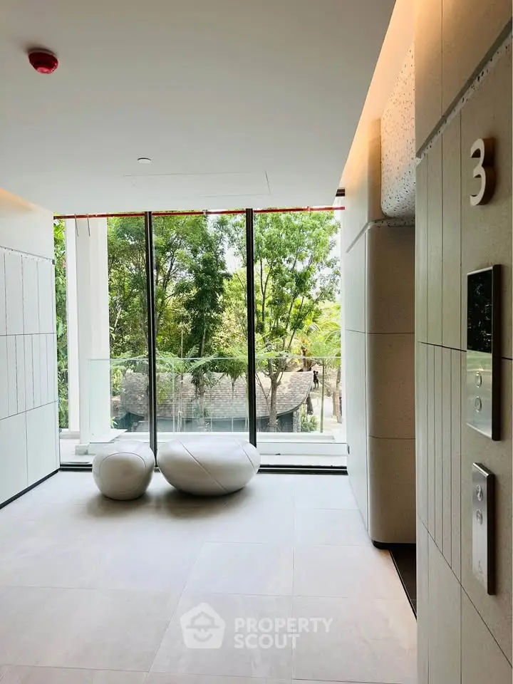 Modern building entrance with sleek design and large windows offering lush green views.