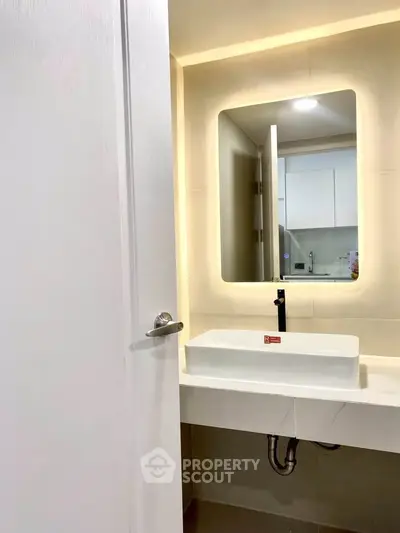 Modern bathroom with sleek sink and illuminated mirror in contemporary apartment.