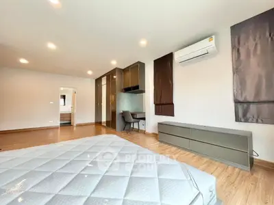 Spacious modern bedroom with wooden flooring, built-in wardrobe, and air conditioning.