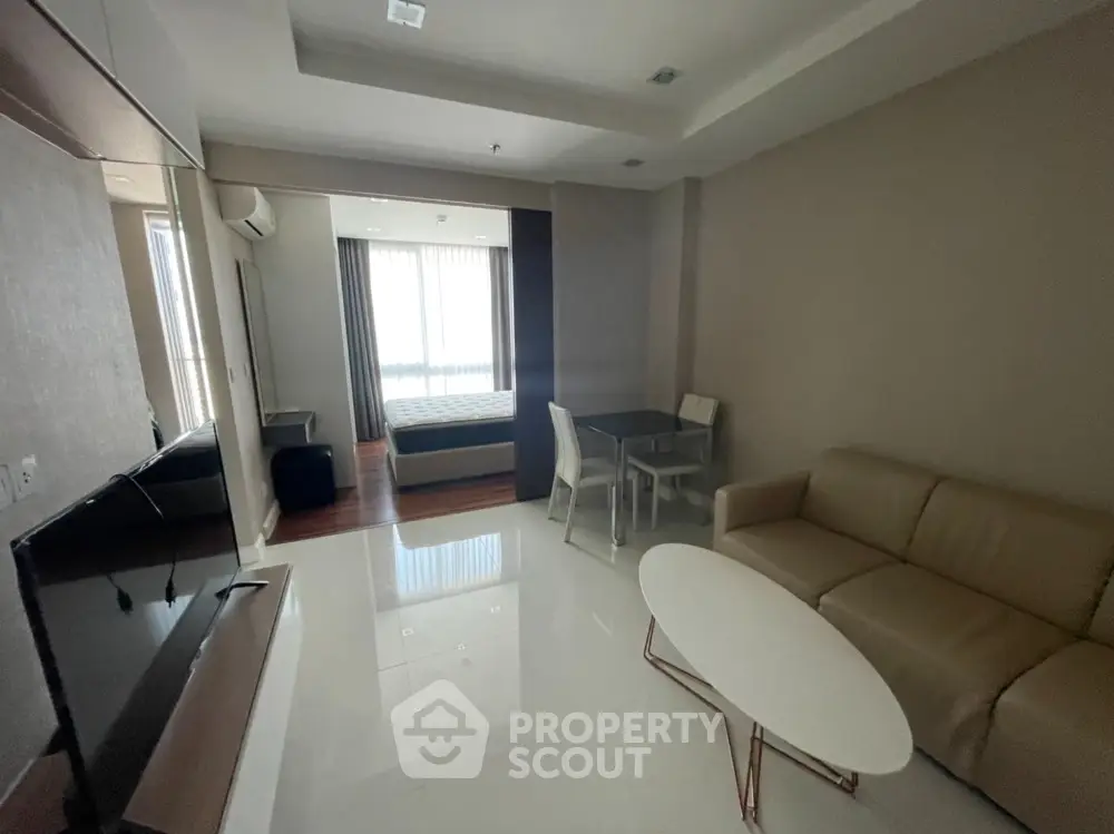 Modern living room with sleek furniture and open layout leading to a cozy bedroom.