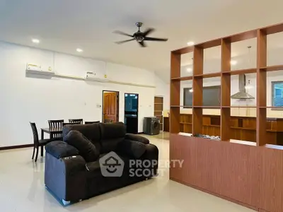 Spacious open-plan living room with modern furniture and dining area, featuring a ceiling fan and stylish partition.