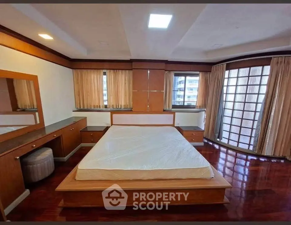 Spacious bedroom with large windows and wooden flooring in a modern apartment.