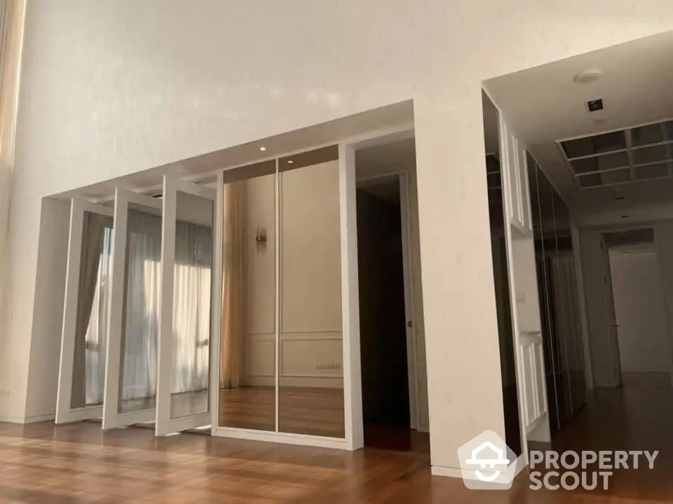 Spacious and well-lit corner unit with gleaming hardwood floors, featuring large mirrored closets and an open layout leading to a modern kitchen.