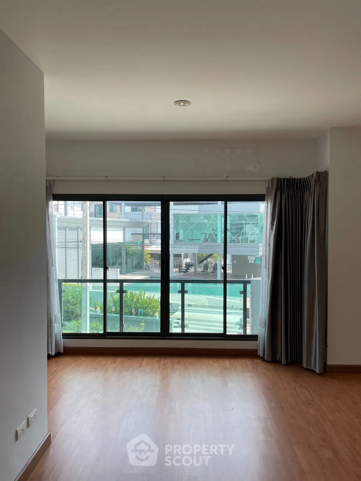 Spacious living room with large window and wooden flooring, offering a bright and airy atmosphere.
