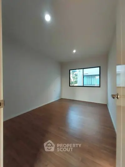 Spacious empty room with wooden flooring and large window, perfect for customization.