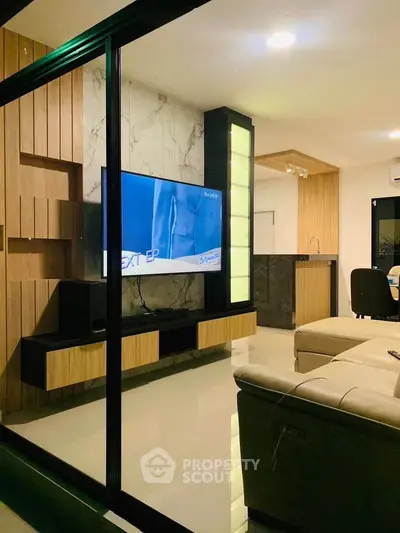 Modern living room with sleek TV setup and open kitchen layout, featuring stylish wood and marble accents.