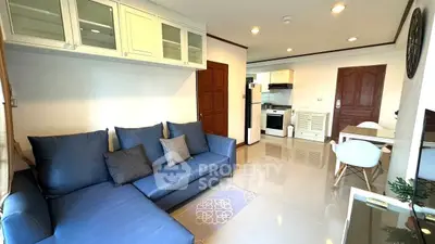 Modern living room with blue sofa, open kitchen, and dining area in a bright apartment.