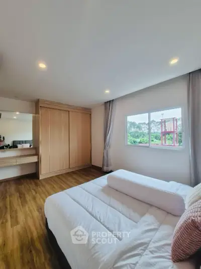 Spacious bedroom with wooden flooring and large window offering natural light.