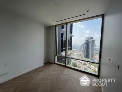 Spacious high-rise corner unit with large windows offering a panoramic city view, herringbone wood flooring, and ample natural light.