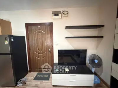 Cozy living room with modern decor, featuring a sleek TV stand, wall shelves, and a welcoming entrance.