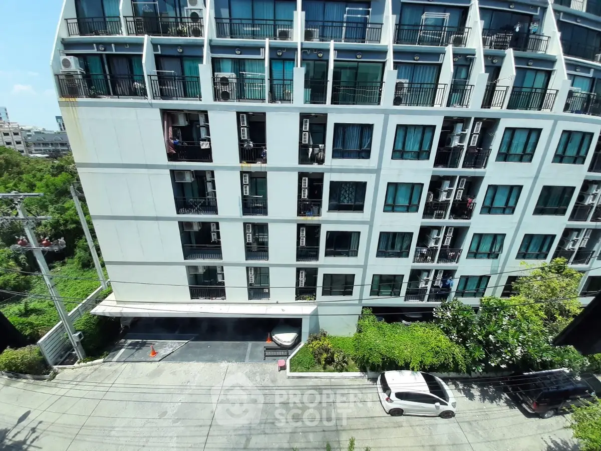 Modern multi-story apartment building with balconies and parking area in urban setting.