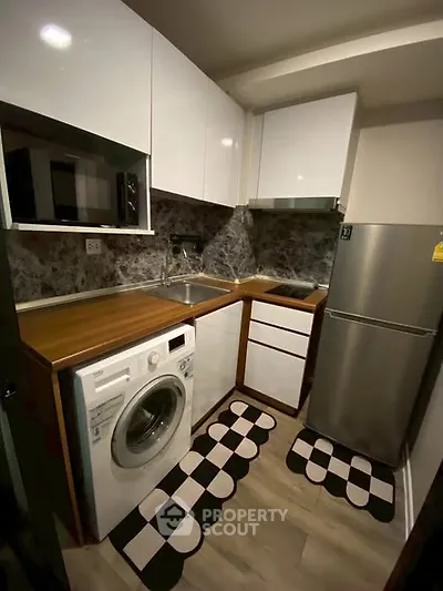 Compact modern kitchen with washing machine and fridge, featuring sleek white cabinets and stylish backsplash.