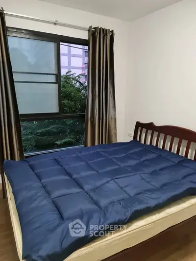 Cozy bedroom with large window and elegant curtains, featuring a comfortable bed with blue bedding.