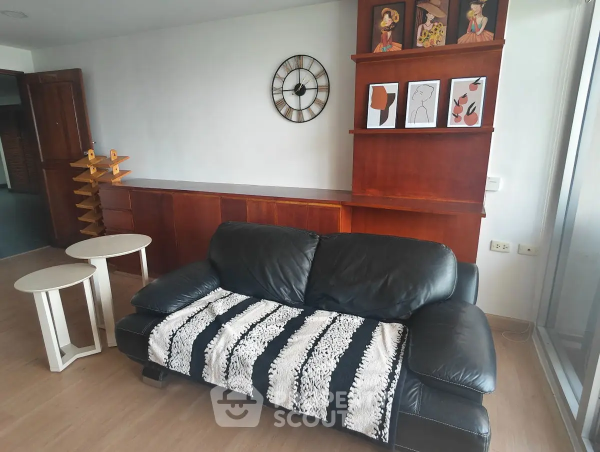 Stylish living room with black leather sofa, modern wall art, and wooden shelving.