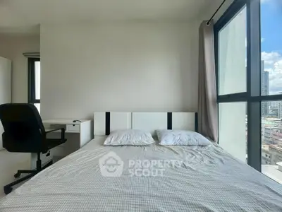 Modern bedroom with large windows offering city views, featuring a comfortable bed and a study desk.