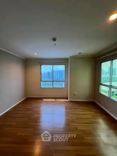 Spacious empty room with large windows offering city views and wooden flooring.