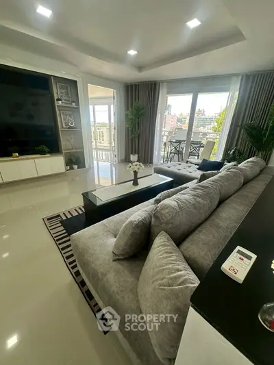 Spacious modern living room with large sofa and balcony view, perfect for relaxation.