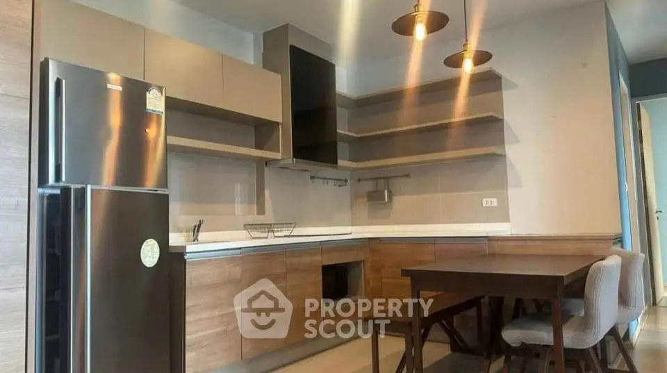 Modern kitchen with sleek cabinets and dining area, featuring contemporary lighting and stainless steel fridge.