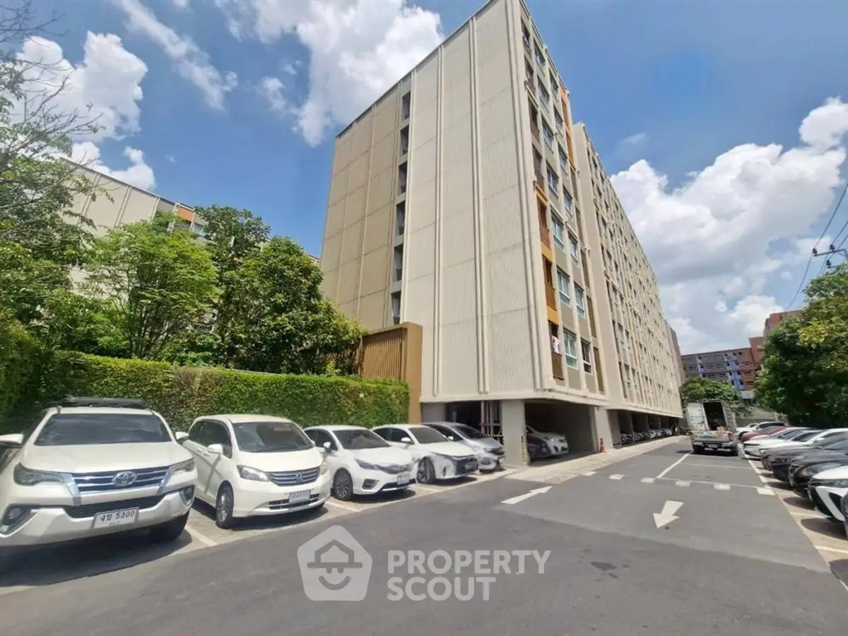 Modern apartment building with ample parking and lush greenery under a clear blue sky.
