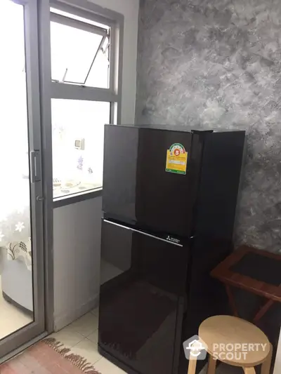 Compact kitchen space featuring a modern black refrigerator, complemented by stylish gray wallpaper and natural light from the window.