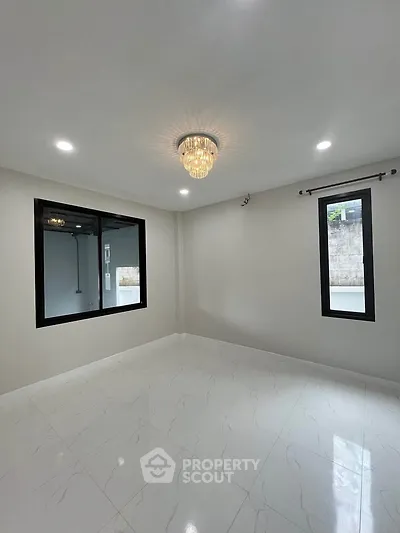 Spacious empty room with elegant chandelier and large windows, perfect for customization.