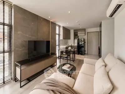 Modern living room with sleek furniture and open kitchen layout, featuring a large TV and stylish decor.