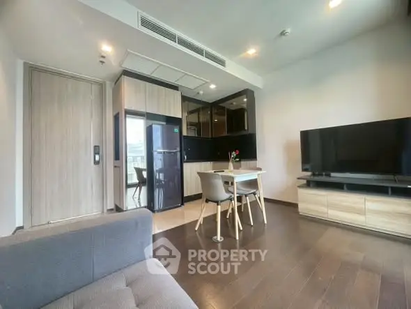 Modern living room with sleek kitchen and dining area, featuring a large TV and stylish furniture.