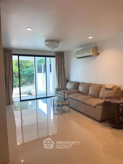 Spacious living room with modern sofa and large windows opening to garden view.