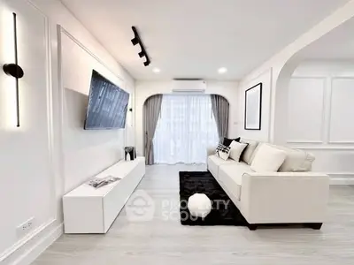 Modern living room with sleek design, featuring a wall-mounted TV, elegant sofa, and large window for natural light.