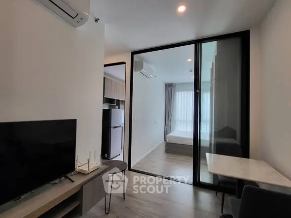 Modern apartment interior with glass partition, sleek furniture, and natural light.