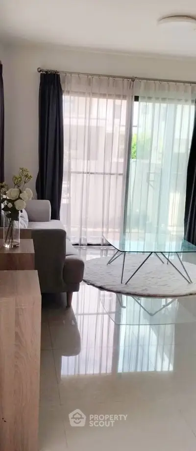 Modern living room with glass coffee table and floor-to-ceiling windows offering natural light.